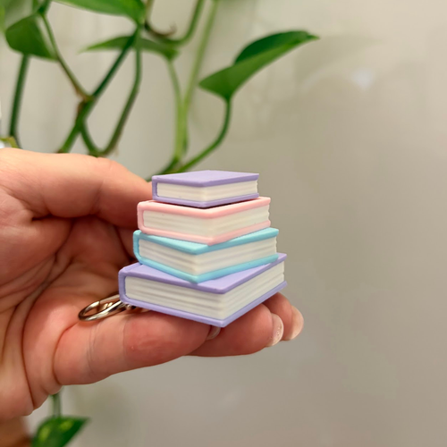Stack of miniature books with pastel covers held in a hand against a blurred green plant background