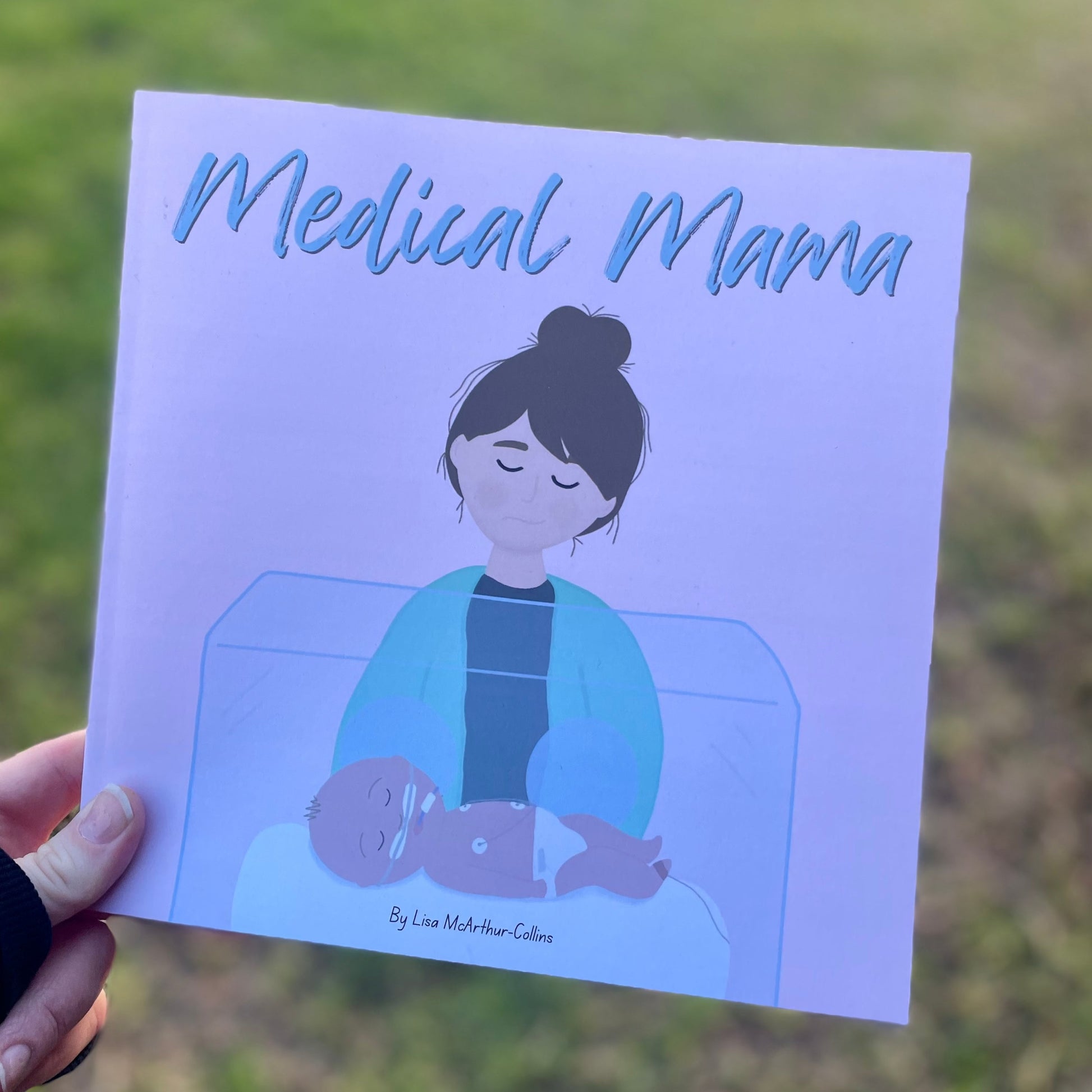 A picture book called Medical Mama being held up against a green grass background