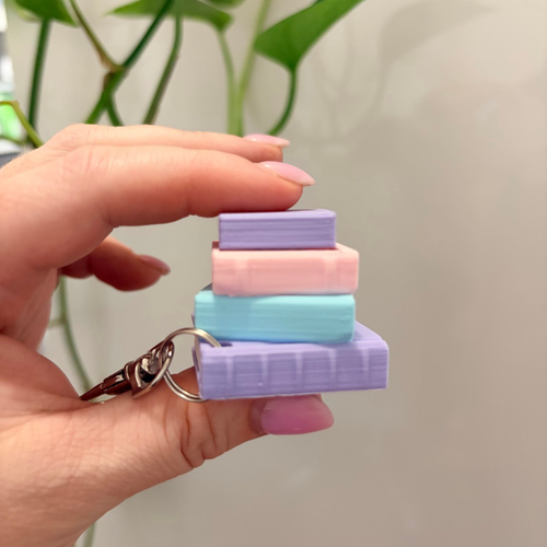 Stack of colorful square keychains held by a hand with a plant in the background