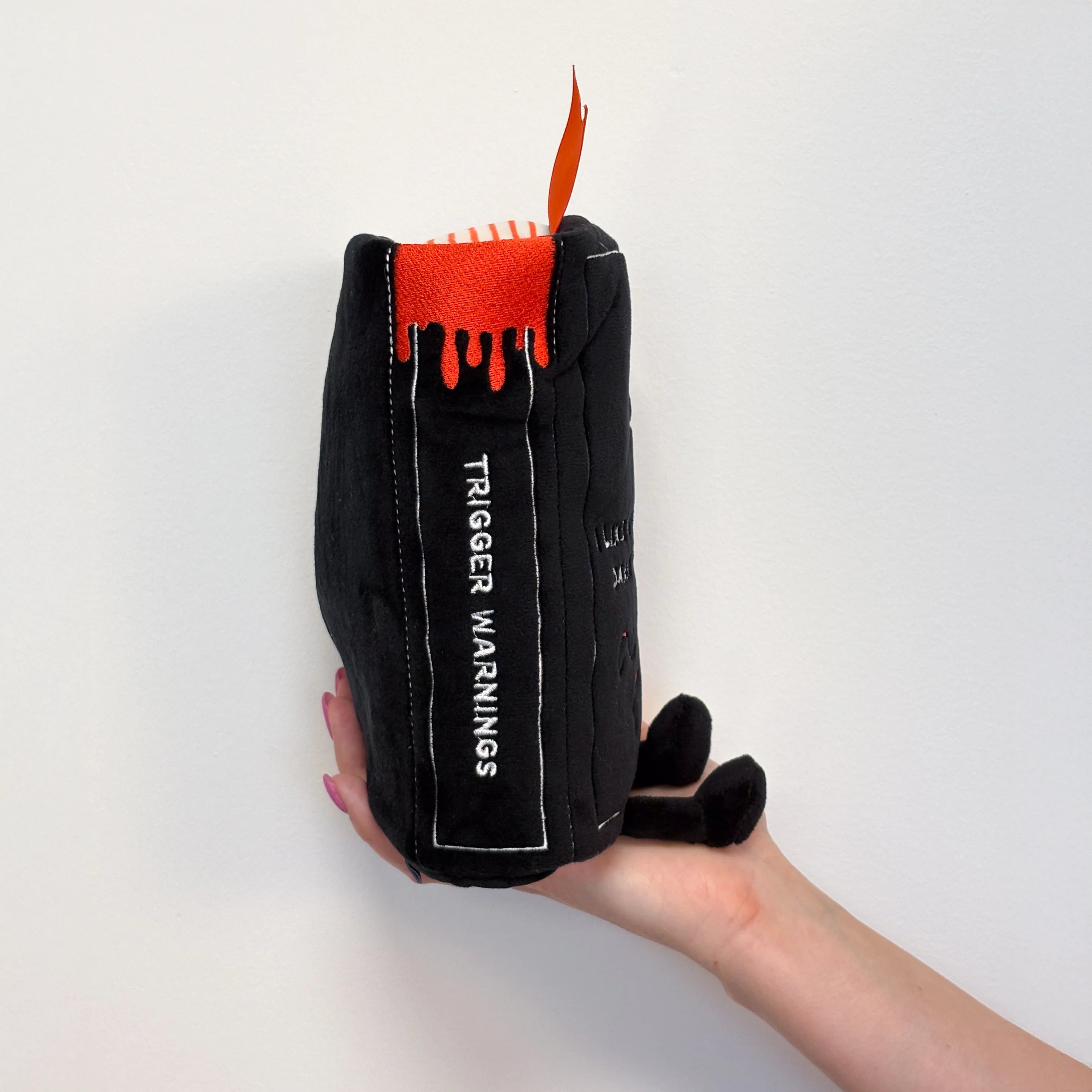 Black plush toy with orange interior held by a hand on a white background